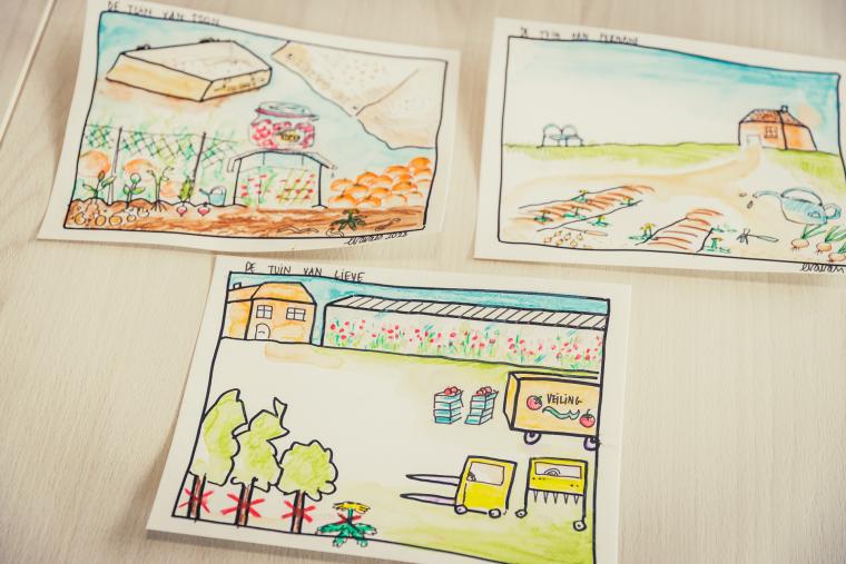 Drie tekeningen van verschillende moestuinen liggen op een witte tafel.