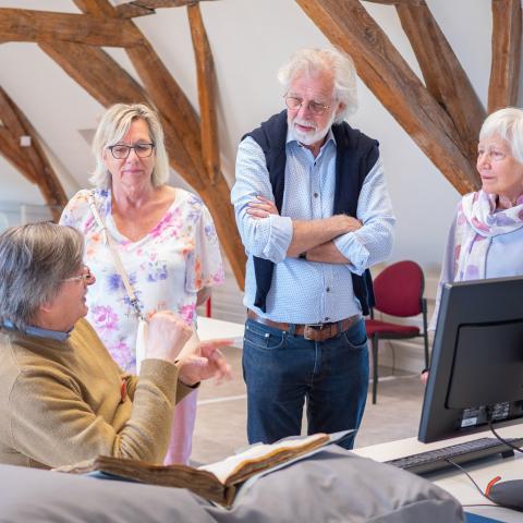 Een vrijwilliger doet uitleg bij zijn werk in het Stadsarchief. Drie bezoekers luisteren aandachtig.