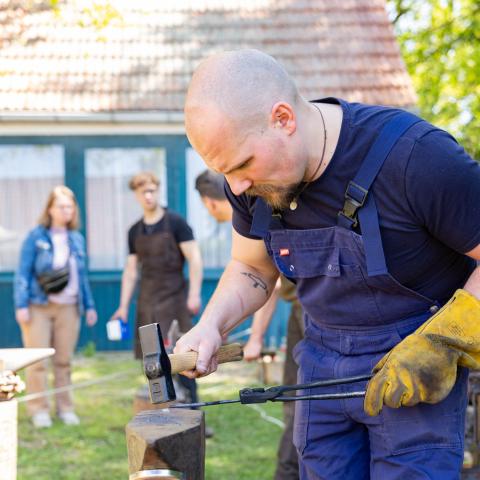 Smid demonstreert het slaan van metaal met hamer op aambeeld.