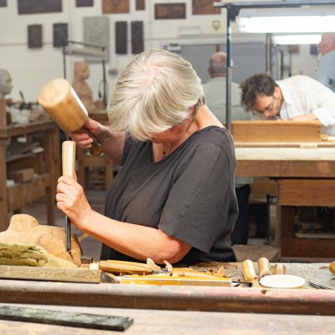 Houtbewerkster aan het werk in het atelier. Ze slaat met een grote hamer op een beitel.