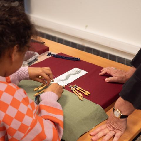 Een jong meisje waagt zich aan het kantklossen van een slang