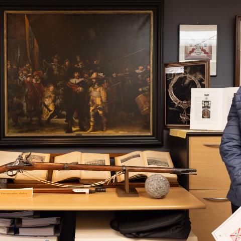 Tentoonstelling bij de Mechelse Kolveniersgilde. Op de achtergrond is een groot schilderij te zien met daarop Kolveniers, op de voorgrond enkele oude boeken en een geweer